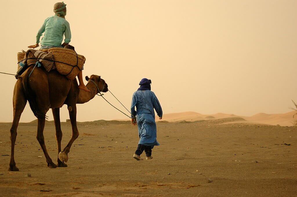 A berber man takes a tourist for a camel ride through in the Western Sahara